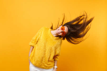 Cheerful young girl in fur sweater and heart orange glasses fooling around in studio, jumping with...