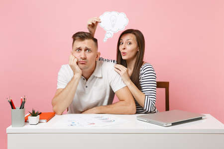 Two fun business woman man colleagues sit work at white desk with idea lightbulb cloud, laptop isolated on pastel pink background. Achievement career concept. Copy space advertising, youth co workingの写真素材