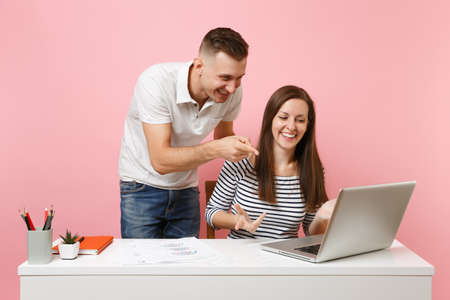 Two young smiling business woman man colleagues sit work at white desk with contemporary laptop isolated on pastel pink background. Achievement career concept. Copy space advertising youth co workingの写真素材