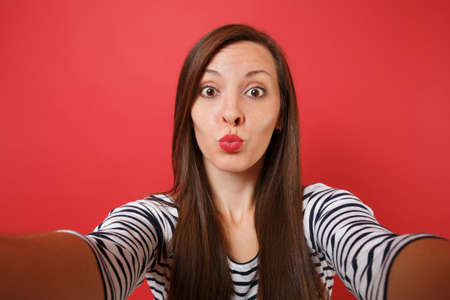 Close up selfie shot of funny young woman in casual striped clothes blowing kisses send air kiss...
