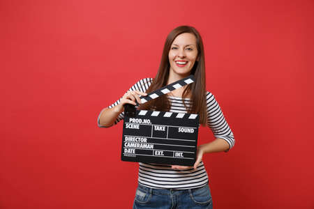 Portrait of attractive young woman in striped clothes holding classic black film making clapperboard...
