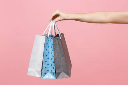 Close up female holds three colored clear empty blank craft paper gift bag for purchases after shopping isolated on pastel pink background. Packaging template mockup Delivery concept advertisingの写真素材
