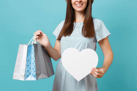 Portrait fashionable beautiful woman in summer dress, straw hat holding packages bags with purchases after shopping, white heart with copy space for advertisement isolated on blue pastel backgroundの写真素材