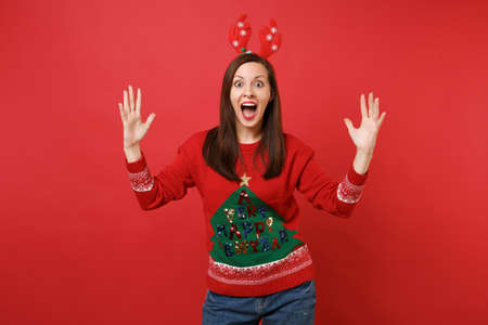 Excited young Santa girl in decorative deer horns on head spreading hands, keeping mouth wide open,...
