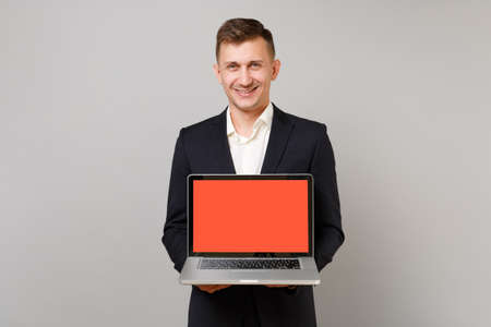 Smiling young business man in classic black suit, shirt holding laptop pc computer with blank empty...
