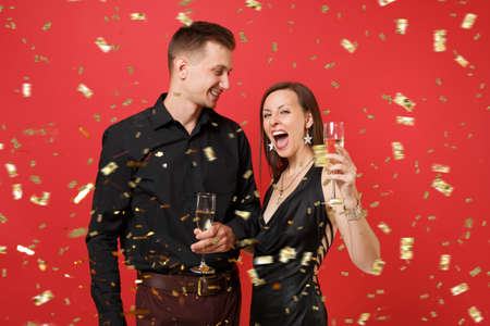 Stunning young couple in black clothes celebrating birthday holiday party with champagne isolated on bright red background. St. Valentine International Women Day Happy New Year 2019 concept. Mock upの写真素材