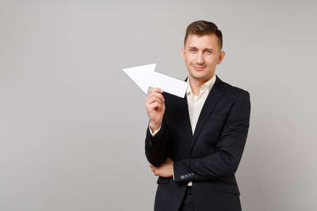 Portrait of attractive young business man in classic black suit, shirt showing aside with arrow...