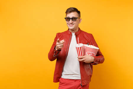 Portrait vogue young man in 3d glasses, leather jacket, t-shirt watching movie film, holding popcorn, cup of soda isolated on bright yellow background. People sincere emotions lifestyle concept.の写真素材