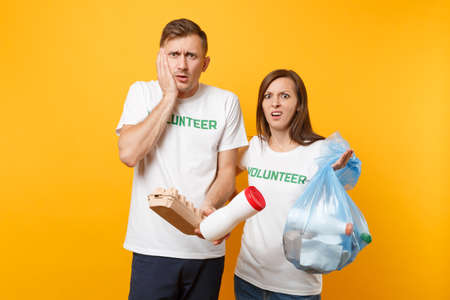 Colleagues couple in t-shirt volunteer trash bag isolated on yellow background. Assistance help charity grace teamwork. Environmental pollution problem. Stop nature garbage environment protectionの写真素材