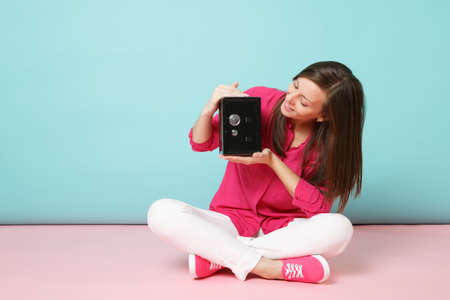 Full length portrait of woman in rose shirt white pants sit on floor hold bank safe for money...