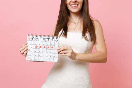 Cropped image of bride woman in white wedding dress holding female periods calendar for checking menstruation days isolated on pink background. Medical, healthcare, gynecological concept. Copy spaceの写真素材
