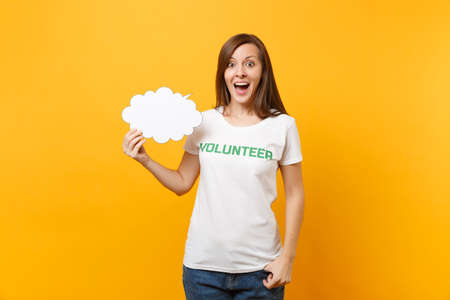 Woman in white t-shirt with written inscription green title volunteer hold empty blank Say cloud speech bubble isolated on yellow background. Voluntary free assistance help charity grace work conceptの写真素材