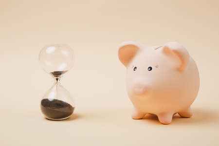 Close up of pink piggy money bank and sandglass isolated on pastel beige wall background. Money...