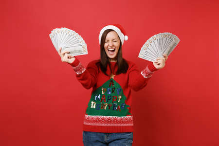 Happy Santa girl with closed eyes screaming, holding lots bunch of dollars banknotes, cash money...