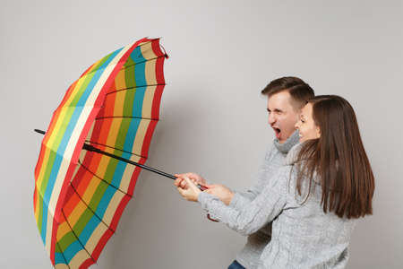 Couple girl guy in gray sweaters scarves together under umbrella isolated on grey wall background, studio portrait. Healthy lifestyle sick disease treatment cold season concept. Mock up copy spaceの写真素材