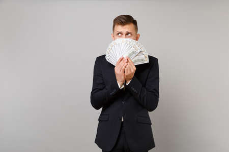 Guilty young business man in suit hiding, covering face with lots bunch of dollars banknotes, cash money isolated on grey background. Achievement career wealth business concept. Mock up copy spaceの写真素材