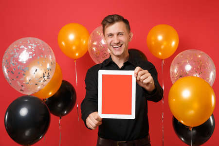 Laughing young man in black classic shirt holding tablet pc computer with blank black empty screen...