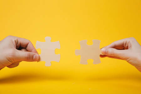 Close up cropped photo of hands holding trying to connect couple wooden jigsaw puzzle pieces...