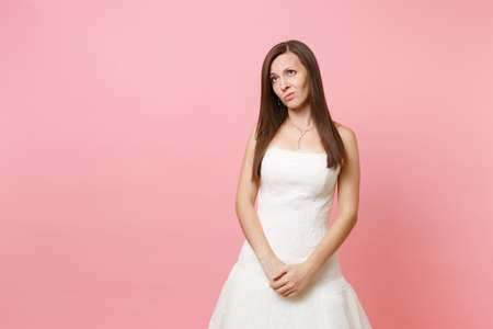 Portrait of concerned upset bride woman in white wedding dress standing holding hands crossed in front of her isolated on pink background. Wedding celebration concept. Copy space for advertisementの写真素材
