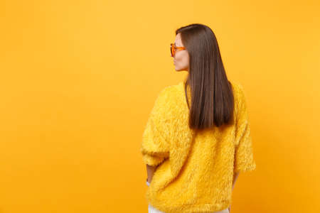 Back rear view of brunette young woman in fur sweater, orange eyeglasses looking aside isolated on...