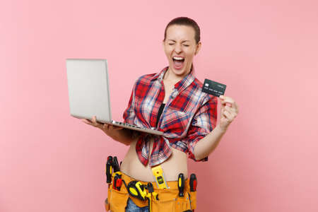 Handyman woman user with kit tools belt full of instruments working on laptop pc computer, holding...