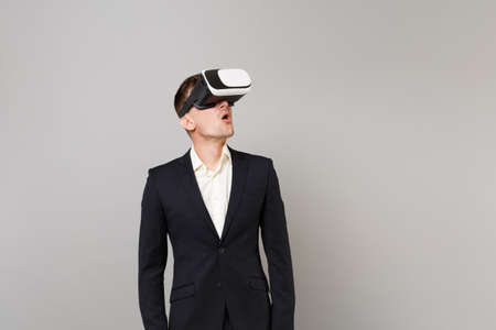 Amazed young business man in classic black suit, shirt looking up in headset, keeping mouth wide...