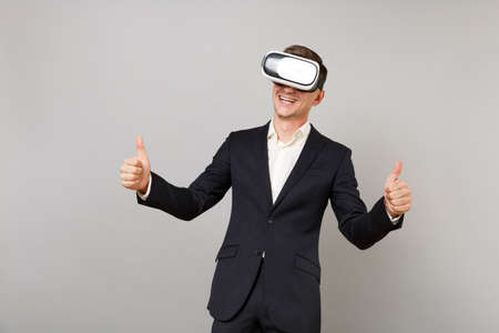 Joyful young business man in classic black suit, shirt looking in headset, showing thumbs up...