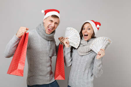 Merry fun couple girl guy in red Santa Christmas hat gray sweaters scarves isolated on grey wall background, studio portrait. Happy New Year 2019 celebration holiday party concept. Mock up copy spaceの写真素材