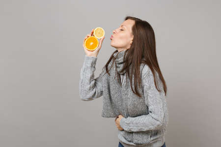 Side view of woman in sweater, scarf blowing sending air kiss to lemon, orange isolated on grey background. Healthy fashion lifestyle, people sincere emotions, cold season concept. Mock up copy spaceの写真素材