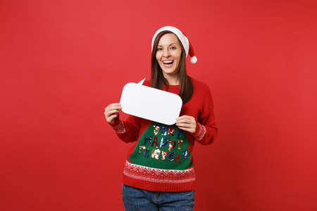 Cute merry young Santa girl in sweater, Christmas hat holding empty blank Say cloud speech bubble isolated on red background. Happy New Year 2019 celebration holiday party concept. Mock up copy spaceの写真素材
