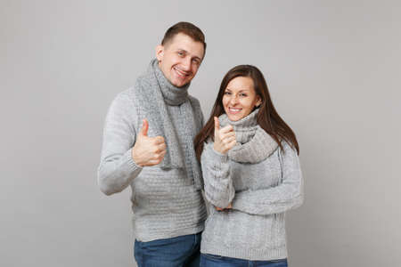 Young cute couple girl guy in gray sweaters, scarves together isolated on grey wall background, studio portrait. Healthy lifestyle, ill sick disease treatment, cold season concept. Mock up copy spaceの写真素材