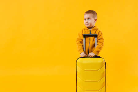 Little traveler tourist kid boy 3-4 years old isolated on yellow orange wall background studio. Passenger traveling abroad to travel on weekends getaway. Air flight journey concept. Mockup copy spaceの写真素材