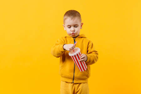Little fun cheerful kid boy 3-4 years old wearing yellow clothes hold cup of soda isolated on orange wall background, children studio portrait. People, childhood lifestyle concept. Mock up copy spaceの写真素材