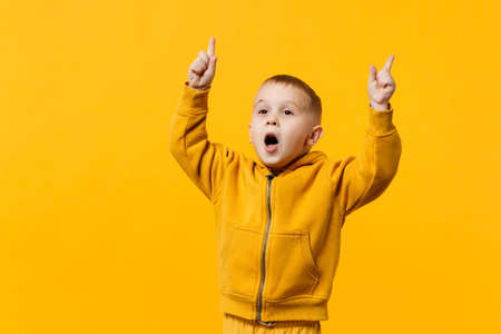 Little cute kid boy 3-4 years old wearing yellow clothes isolated on bright orange wall background, children studio portrait. People sincere emotions, childhood lifestyle concept. Mock up copy spaceの写真素材