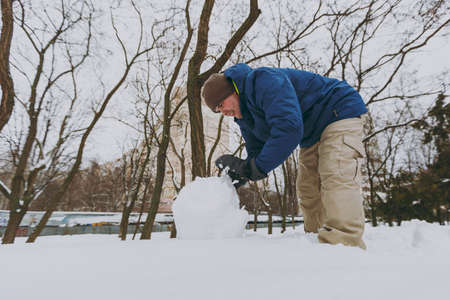 Smiling young man in blue winter warm clothes playing, making snowball, snowman in snowy park or forest outdoors. Winter fun, leisure on holidays. Love relationship family people lifestyle conceptの写真素材