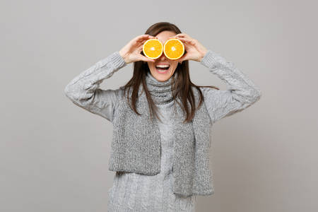 Laughing young woman in gray sweater, scarf covering eyes with oranges isolated on grey wall background. Healthy fashion lifestyle, people sincere emotions, cold season concept. Mock up copy spaceの写真素材