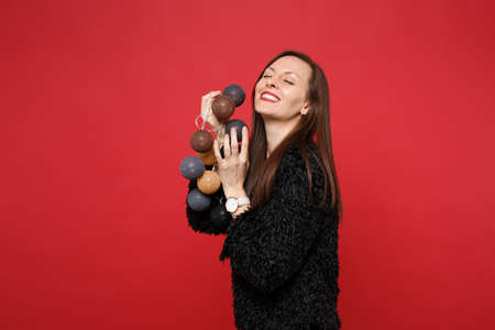 Pretty young woman in black fur sweater keeping eyes closed holding round lights with garlands for...
