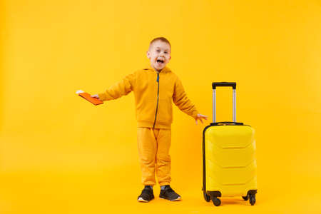 Little traveler tourist kid boy 3-4 years old isolated on yellow orange wall background studio. Passenger traveling abroad to travel on weekends getaway. Air flight journey concept. Mockup copy spaceの写真素材