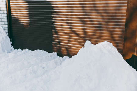 Snow drifts on brown metal garage doors background. Winter urban city seasonの写真素材