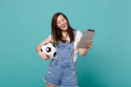Joyful young woman football fan holding soccer ball, using tablet pc computer isolated on blue turquoise wall background. People emotions, sport family leisure lifestyle concept. Mock up copy spaceの写真素材