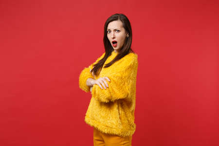 Portrait of irritated disgusted young woman in yellow fur sweater swearing holding hands crossed isolated on bright red wall background. People sincere emotions, lifestyle concept. Mock up copy spaceの写真素材