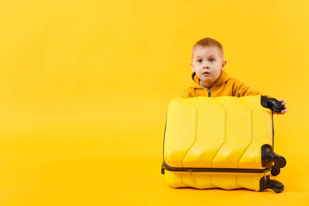 Little traveler tourist kid boy 3-4 years old isolated on yellow orange wall background studio. Passenger traveling abroad to travel on weekends getaway. Air flight journey concept. Mockup copy spaceの写真素材