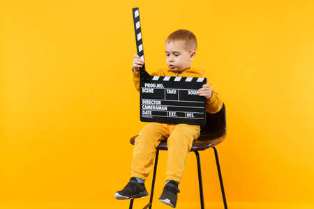 Little kid boy 3-4 years old in yellow clothes isolated on orange wall background, children studio portrait. People childhood lifestyle concept. Hand hold film making clapperboard. Mock up copy spaceの写真素材