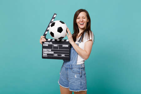 Funny blinking woman football fan support favorite team with soccer ball, classic black film making clapperboard isolated on blue turquoise background. People emotions, sport family leisure conceptの写真素材