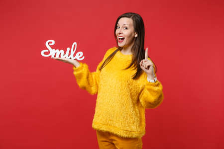 Amazed young woman in fur sweater pointing index finger up with great new idea hold wooden word letters smile isolated on red background. People sincere emotions lifestyle concept. Mock up copy spaceの写真素材