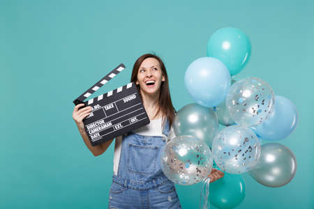 Cheerful woman looking up holding classic black film making clapperboard, celebrating with colorful...