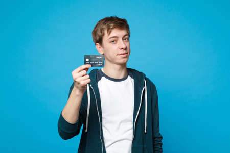 Portrait of handsome young man in casual clothes holding credit bank card isolated on blue wall...