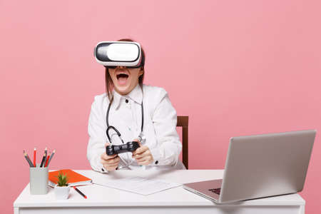 Female doctor sit at desk work on computer with medical document in headset in hospital isolated on...
