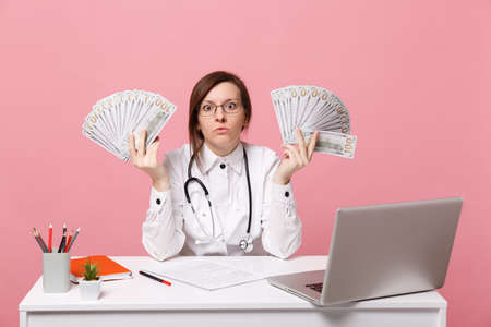 Female doctor sit at desk work on computer with medical document cash money in hospital isolated on...