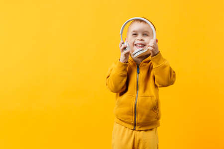Little kid boy 3-4 years old wearing yellow clothes in headphones isolated on orange wall background, children studio portrait. People sincere emotions childhood lifestyle concept. Mock up copy spaceの写真素材